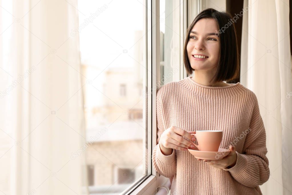 Young woman drinking coffee near window in morning