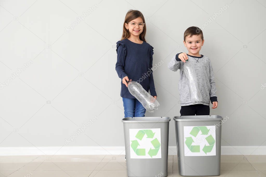 Children throwing garbage into trash bins near light wall. Recycling concept