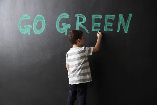Malý chlapec psaní textu Go Green na tmavé stěně — Stock fotografie