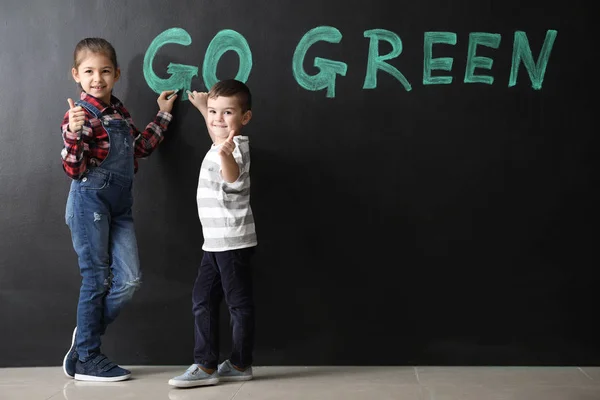Маленькі діти пишуть текст GO GREEN на темній стіні — стокове фото