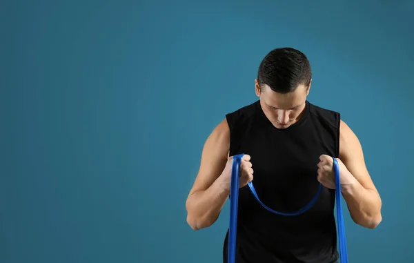 Sporty young man training with resistance band against color background — Stock Photo, Image
