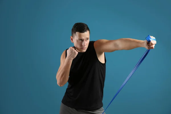 Sporty young man training with resistance band against color background — Stock Photo, Image