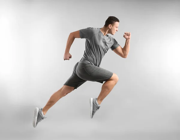 Sporty young man running against grey background — Stock Photo, Image