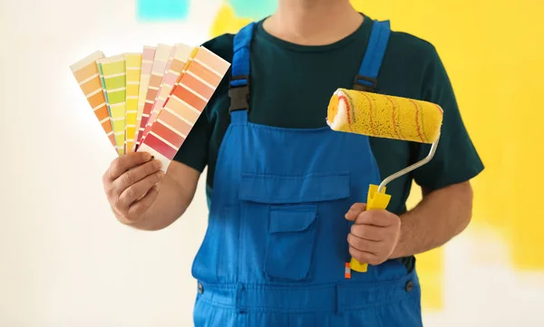 Pintor masculino en uniforme con muestras de paleta de colores y cepillo de rodillo en interiores —  Fotos de Stock
