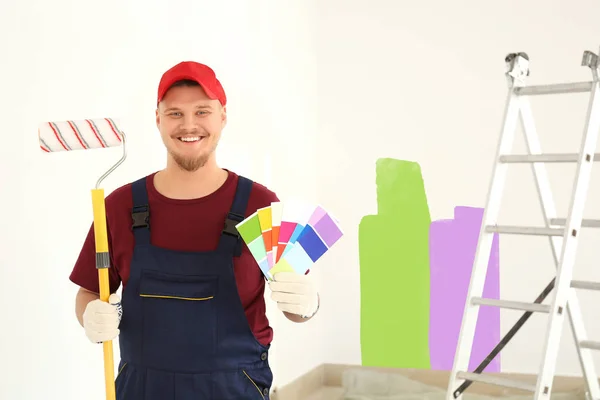 Pintor masculino en uniforme con cepillo de rodillo y muestras de paleta de colores en interiores — Foto de Stock