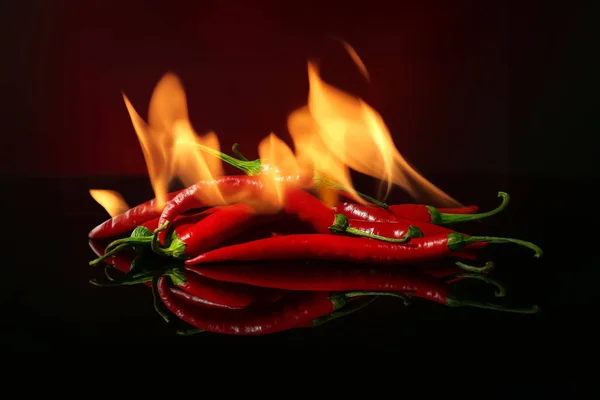 Red hot chili peppers with fire on dark color background — Stock Photo, Image