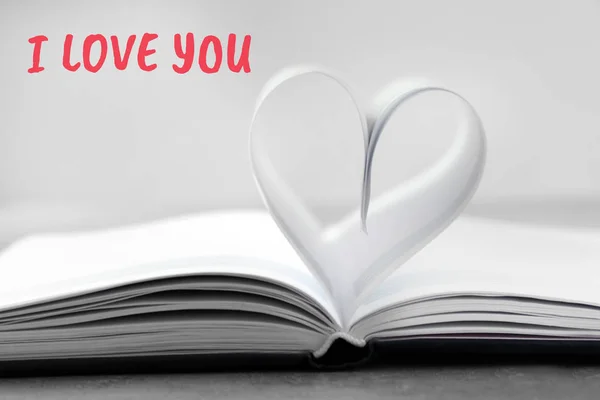 Corazón hecho de hojas de papel sobre libro con texto TE AMO. Celebración de San Valentín — Foto de Stock