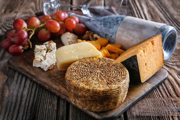 Board with assortment of tasty cheese on wooden table — Stock Photo, Image