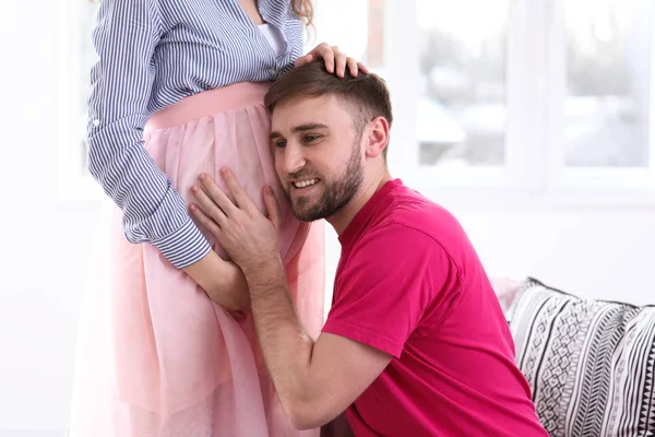 Νεαρός σύζυγος ακούει την κοιλιά της εγκύου γυναίκας του στο σπίτι — Φωτογραφία Αρχείου