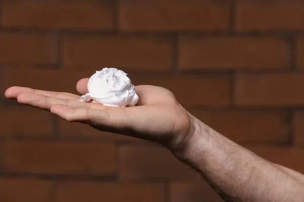 Male hand with shaving foam against brick wall