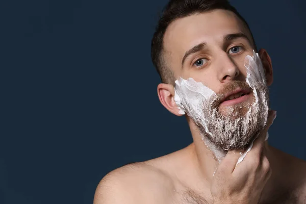 Bearded man applying shaving foam on dark background