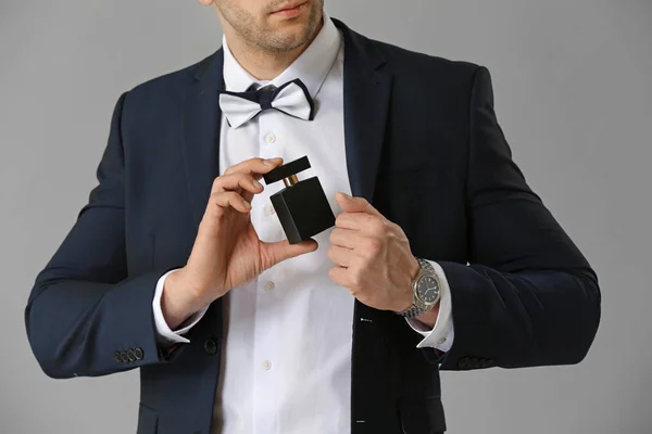 Handsome man with bottle of perfume on grey background — Stock Photo, Image