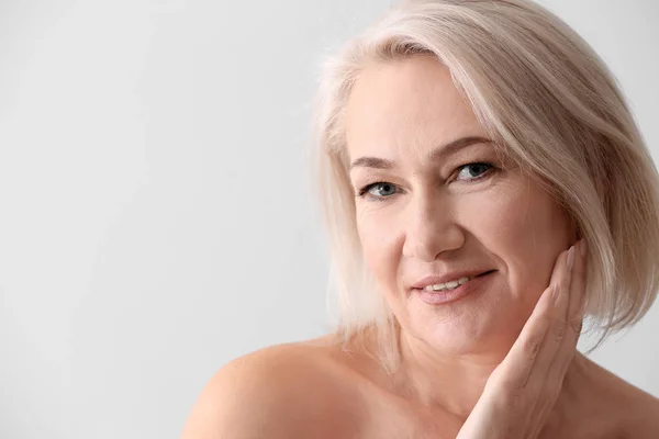 Mature woman giving herself face massage on light background — Stock Photo, Image