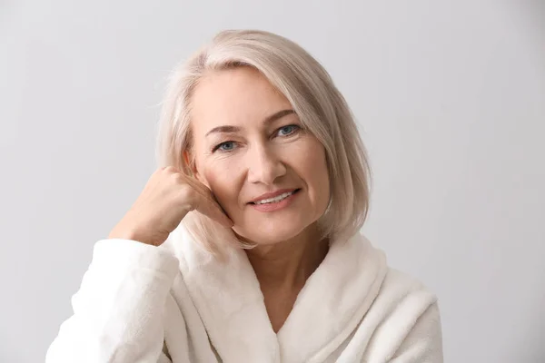 Mature woman giving herself face massage on light background — Stock Photo, Image