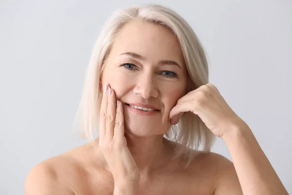 Mujer madura dándose masaje facial sobre fondo claro — Foto de Stock