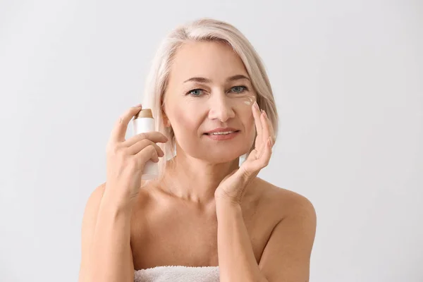 Mujer madura aplicando suero facial sobre fondo claro — Foto de Stock