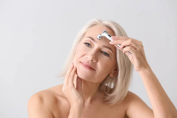 Mujer madura con herramienta de masaje facial sobre fondo claro — Foto de Stock