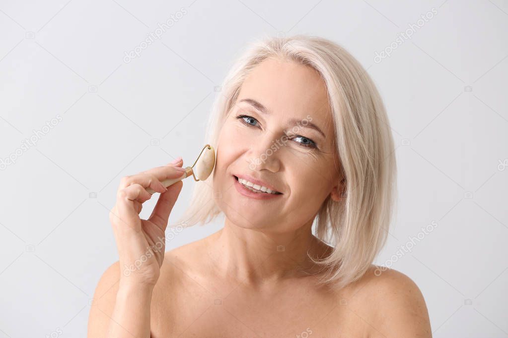 Mature woman with facial massage tool on light background