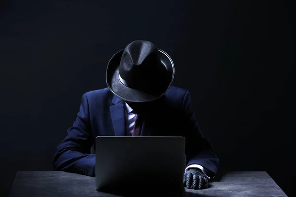 Професійний хакер з ноутбуком, що сидить за столом на темному фоні — стокове фото