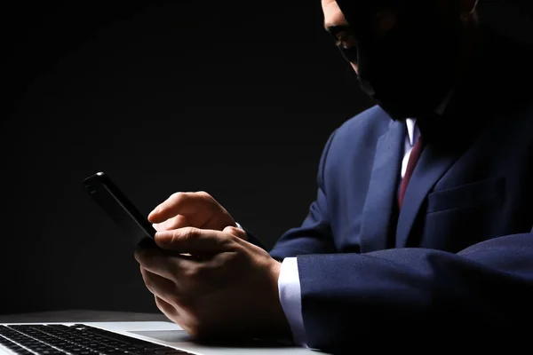 Profi-Hacker mit Laptop und Handy am Tisch vor dunklem Hintergrund — Stockfoto