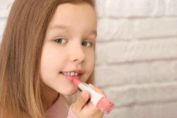 Porträtt av söt liten flicka med läppstift på ljus bakgrund — Stockfoto