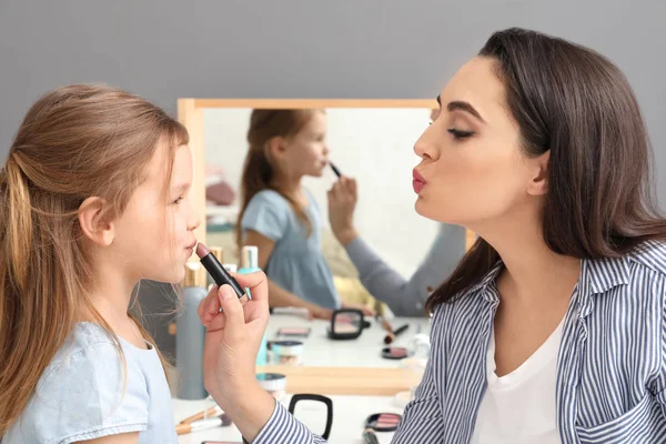 Junge Mutter trägt zu Hause Lippenstift auf die Lippen ihrer Tochter auf — Stockfoto