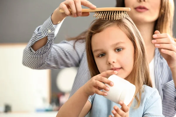 Joven madre cepillando el pelo de su linda hijita en casa — Foto de Stock