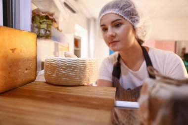 Woman checking tasty cheese on shelf in kitchen clipart