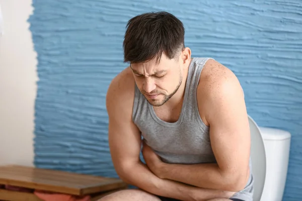 Man suffering from diarrhea while sitting on toilet bowl at home — Stock Photo, Image