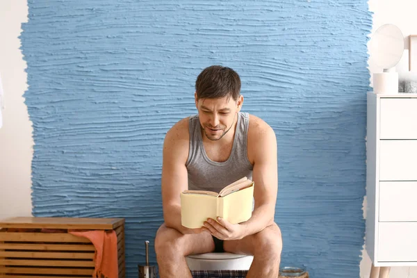 Homem lendo livro enquanto sentado em vaso sanitário em casa — Fotografia de Stock
