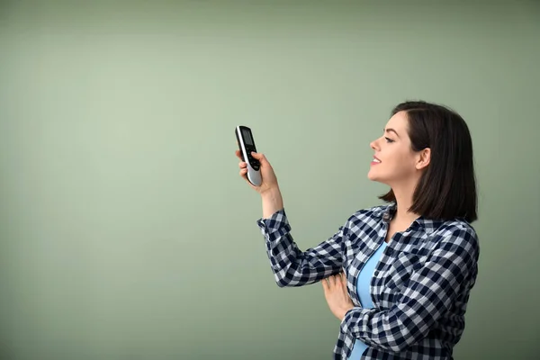 Junge Frau mit Klimaanlage-Fernbedienung auf farbigem Hintergrund — Stockfoto