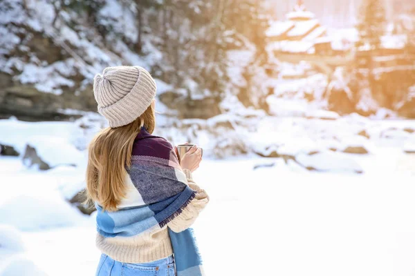 Vacker kvinna med kopp varm glögg på snöiga resort — Stockfoto
