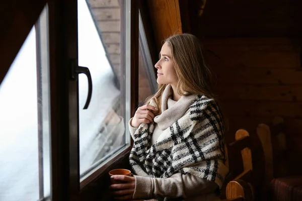 Young woman with hot drink near window on winter day — Stock Photo, Image