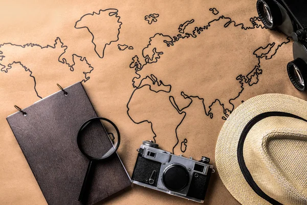 世界地图上的笔记本、照片相机、帽子和放大镜。旅游理念 — 图库照片