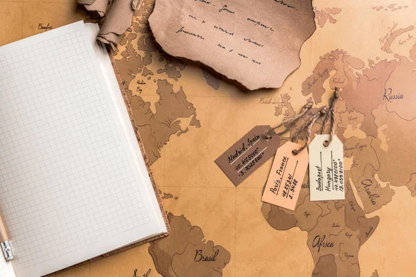 Cuaderno, etiquetas con coordenadas y hoja de papel vieja en el mapa del mundo. Concepto de viaje — Foto de Stock