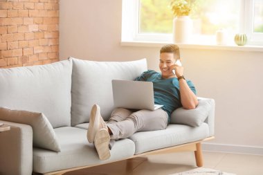 Evde dizüstü bilgisayarda çalışırken telefonla konuşan genç serbest meslek