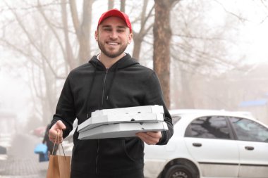 Karton pizza kutuları ve kağıt torba açık havada olan genç adam. Gıda dağıtım hizmeti