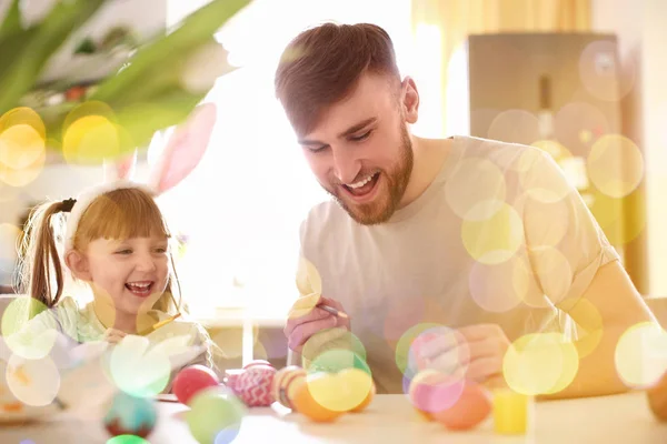 Father painting Easter eggs with his daughter at table