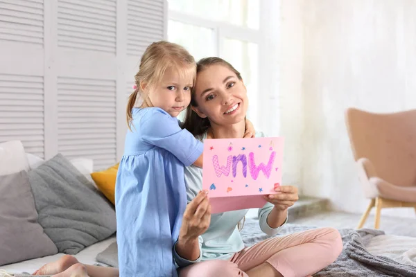 Madre recibiendo tarjeta de felicitación de su linda hija pequeña en casa — Foto de Stock