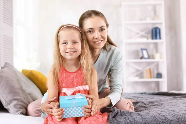 Linda niña con su mamá y caja de regalo sentada en la cama en casa — Foto de Stock
