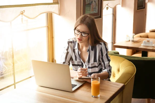 Young female freelancer with laptop and notebook working in cafe — Stock Photo, Image