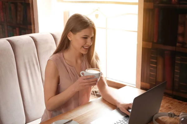 Young female freelancer drinking coffee while working on laptop in cafe — Stock Photo, Image