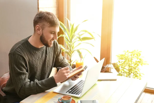 Young freelancer with laptop and notebook working in cafe — Stock Photo, Image