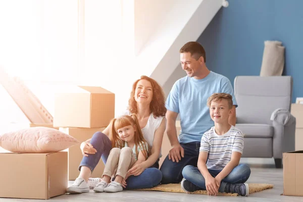 Familia feliz sentada en el suelo cerca de cajas de cartón en su nueva casa —  Fotos de Stock