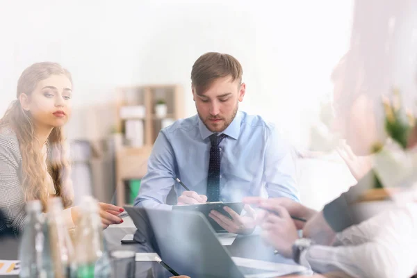 Jóvenes teniendo una reunión de negocios en la oficina, vista a través del vidrio — Foto de Stock