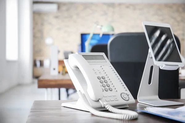 Рабочее место со стационарным телефоном и планшетным компьютером на столе в современном офисе — стоковое фото