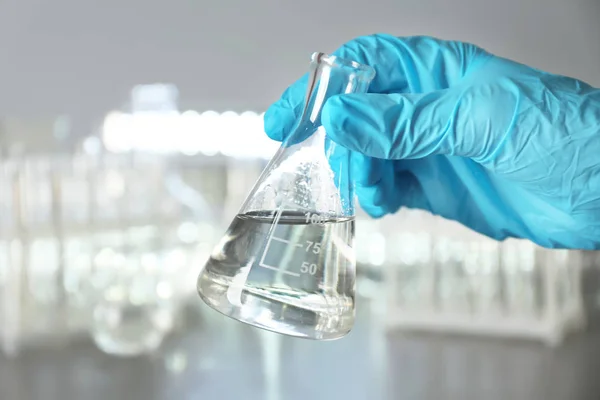 Laboratório trabalhador segurando frasco com água sobre fundo desfocado — Fotografia de Stock