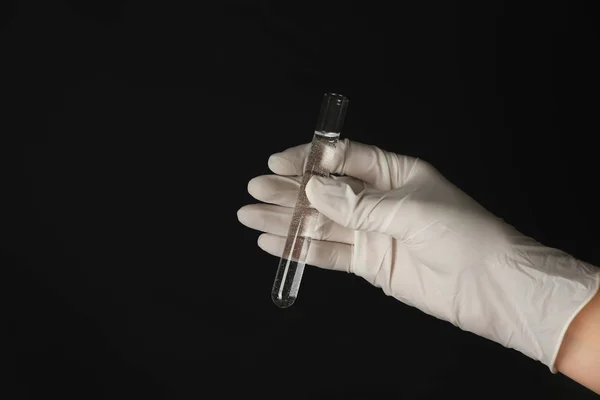 Laborangestellte hält Reagenzglas mit Wasser auf schwarzem Hintergrund — Stockfoto