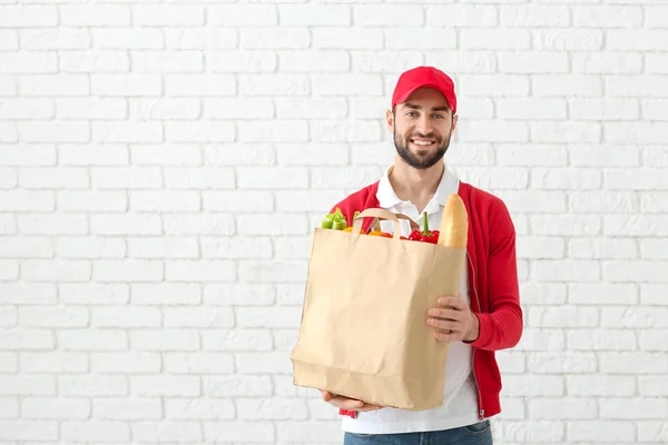 Delivery man holding paper bag with food on brick wall background