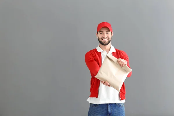 Delivery man holding paper bag with food on grey background — Stock Photo, Image